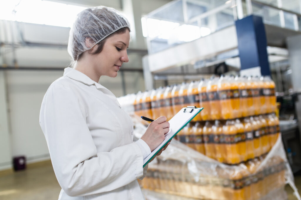 Young happy female worker in bottling factory checking juice bottles before shipment. Inspection quality control.